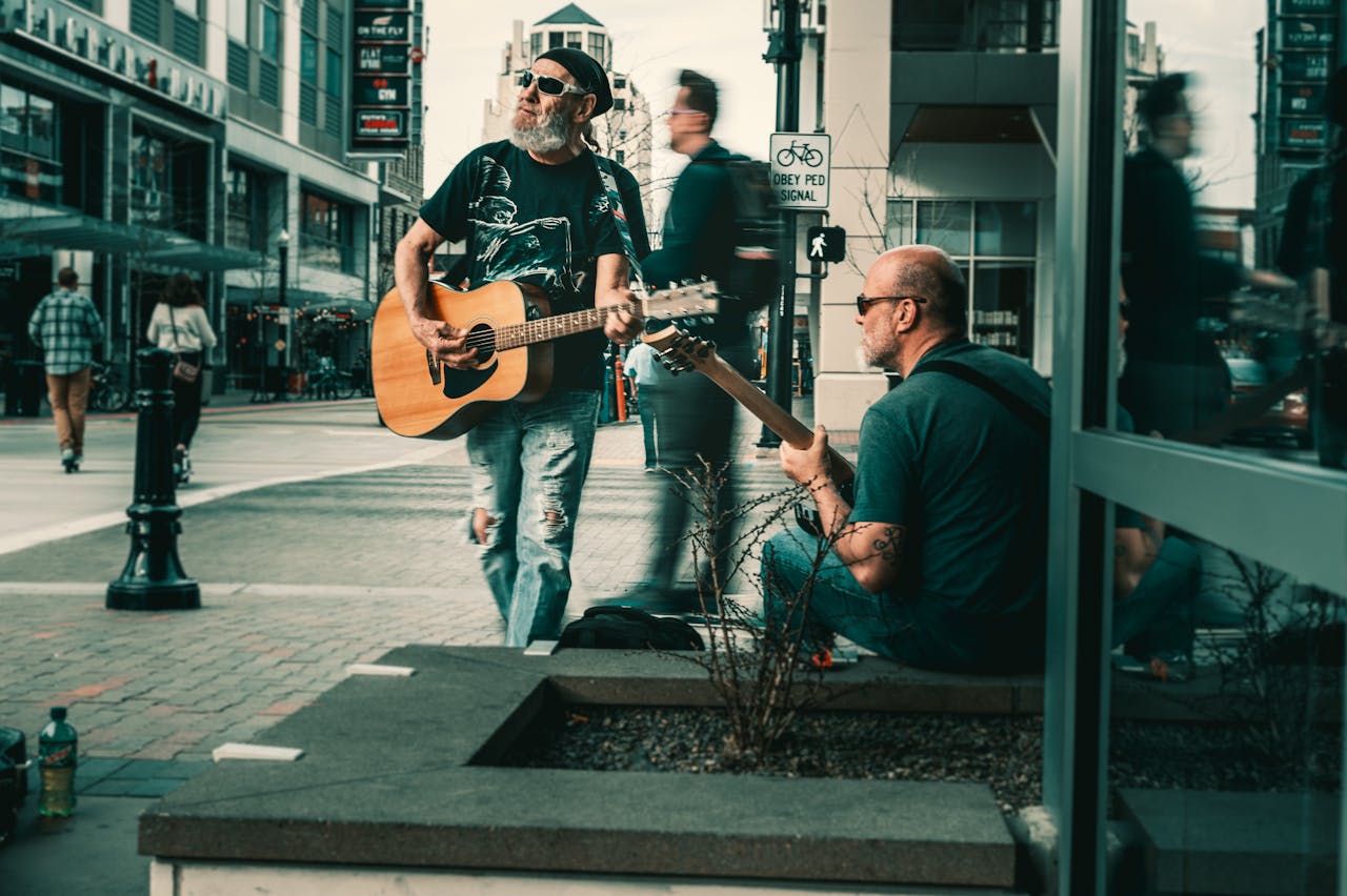 Two male musicians perform on a city street with guitars in a lively urban environment.