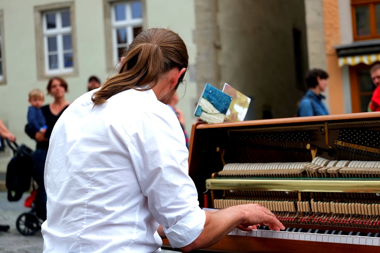 Musician performing on a street with an upright piano, engaging passersby.